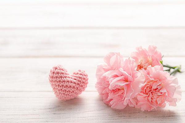 A wooden background with a knitted heart and a bunch of flowers. 