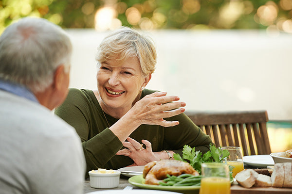 A senior woman laughs and talks to a senior man at lunch outside. 