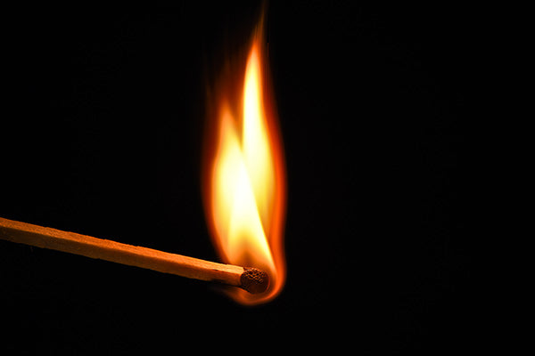 A lit match with fire against a dark background. 