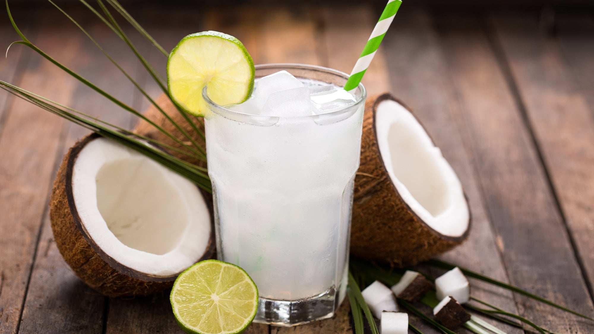 Glass of coconut water surrounded by coconuts and limes